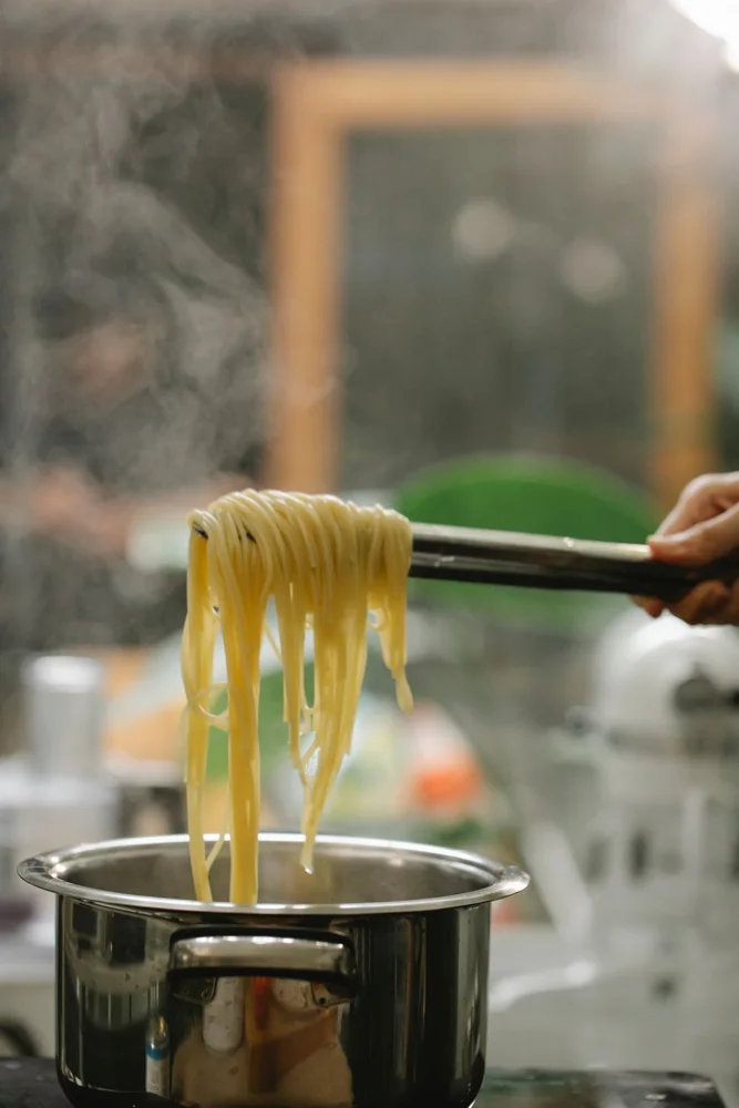 Crop anonymous chef picking freshly cooked Italian spaghetti with tongs from saucepan while serving food in kitchen