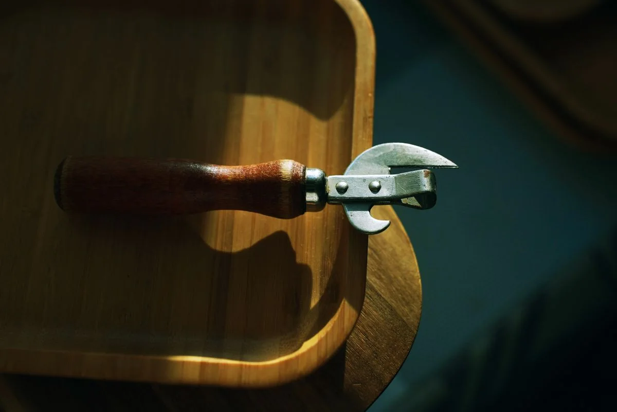 Rustic vintage can opener on a wooden tray, bathed in warm sunlight.
