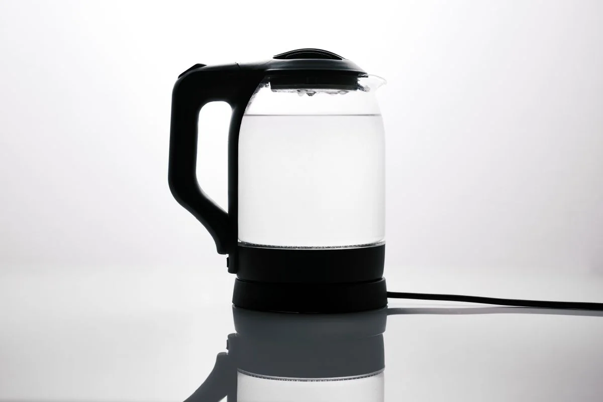Sleek glass electric kettle with water, reflecting on a glossy surface, ideal for modern kitchens.