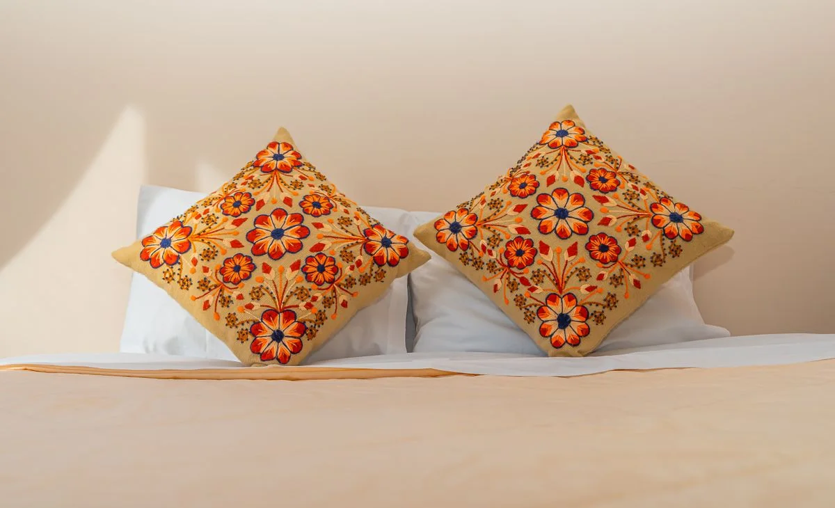 Colorful floral cushions with intricate embroidery on a bed in a bright, modern room.