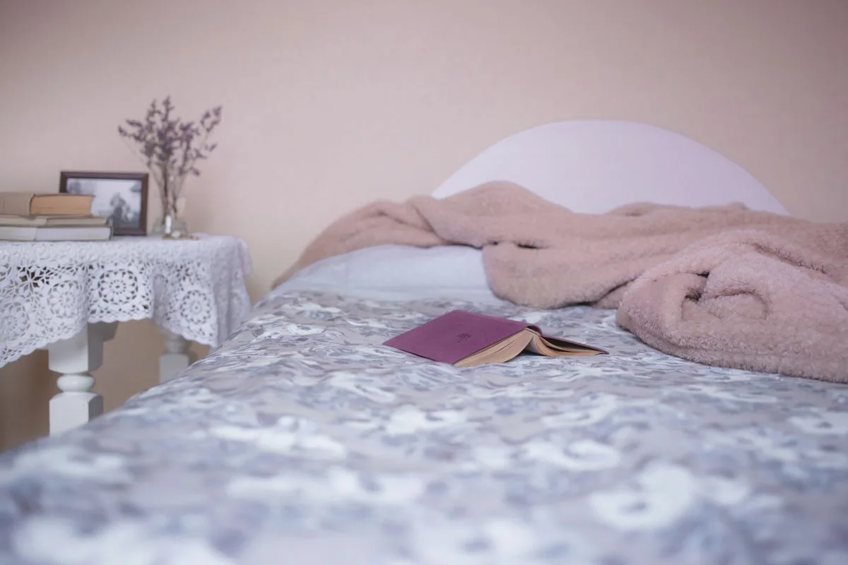 A cozy bedroom interior with a comfortable bed, open book, and lace-covered table for relaxation.