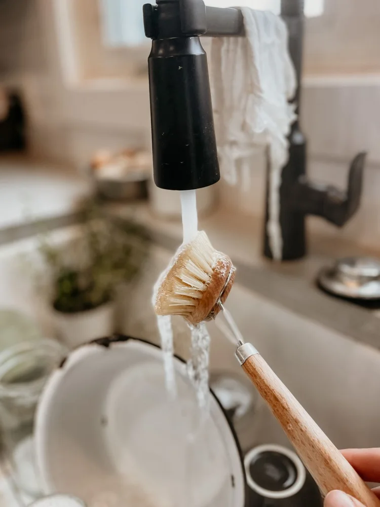 Close-up of brush cleaning a dish in a modern kitchen sink with running water.