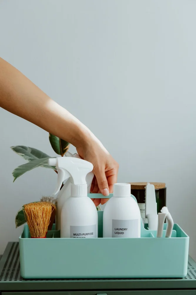Hand arranging cleaning products in a tidy organizer, promoting cleanliness and order.