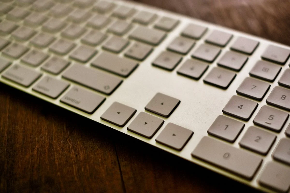 Stylized close-up of a modern white keyboard placed on a wooden desk.