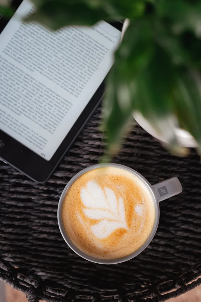 Aerial view of cappuccino and eReader on a dark woven table, perfect for relaxing moments.