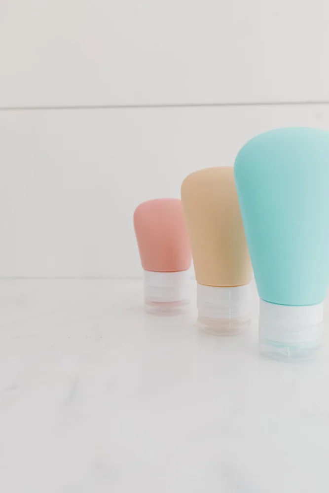Minimalist composition of pastel travel bottles on a white marble surface.
