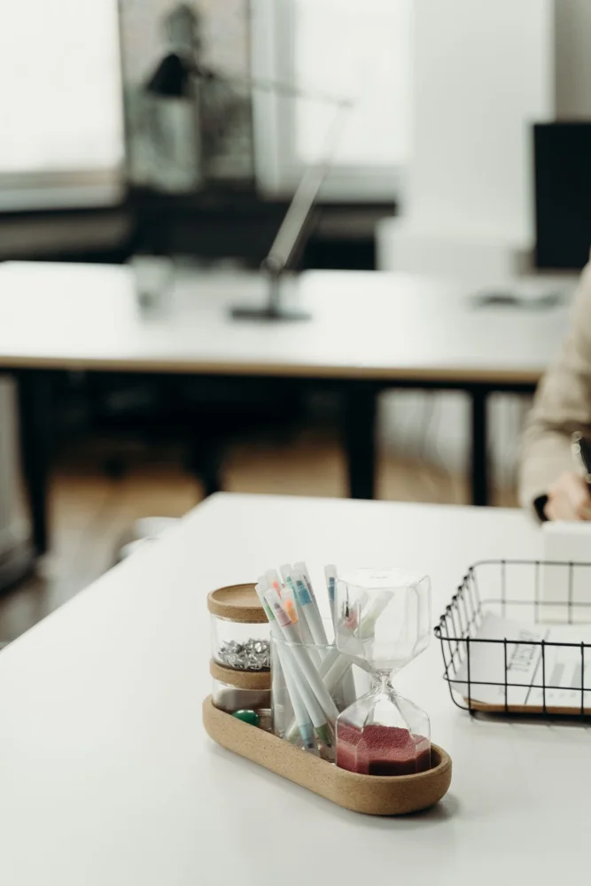 A neatly organized office desk featuring a tray with markers, an hourglass, and paperclips.