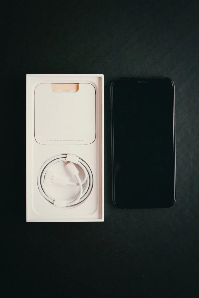 Minimalist image of a smartphone and its charging cable in an open box on a black background.
