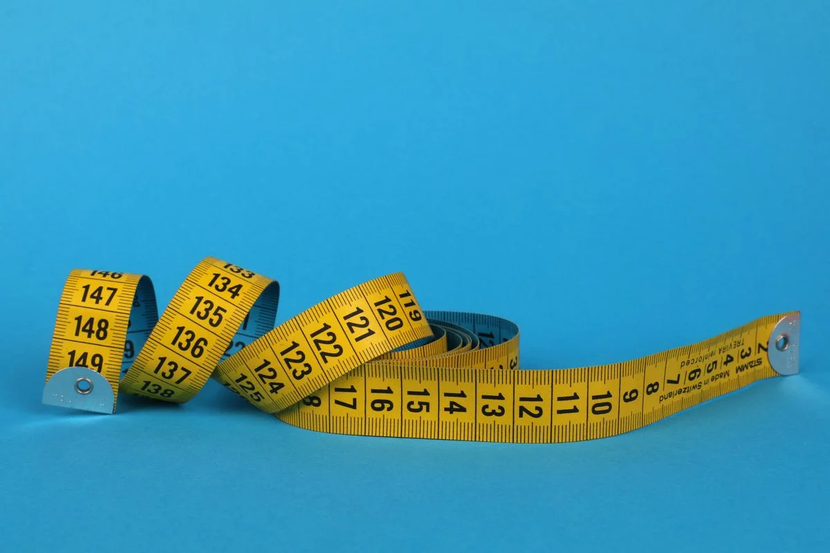 Coiled yellow measuring tape against a vibrant blue background, offering ample copy space.
