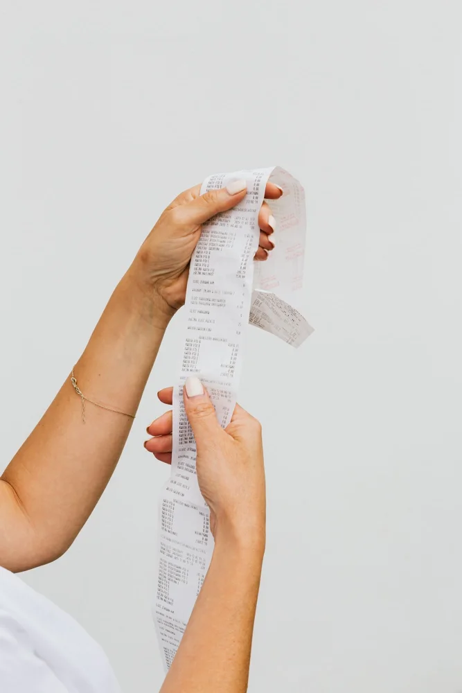 Close-up of woman's hands holding a long receipt against a white background, representing shopping or budgeting.