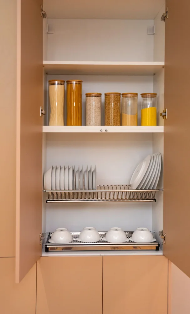 Neatly organized kitchen cupboard showcasing dishes and dry goods in jars.