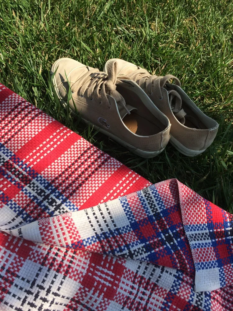 A casual outdoor picnic scene featuring shoes and a colorful blanket on green grass.